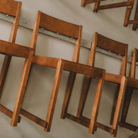 Stacked wooden chairs in a warm brown finish against a neutral background, showcasing clean lines and minimalist design.