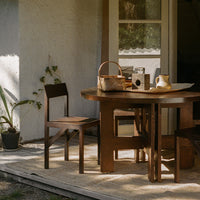 "Rustic brown wooden table with matching chairs, set against a natural outdoor backdrop."