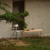 Light wood table with a smooth finish, paired with a sleek silver metal chair against a textured gray wall.