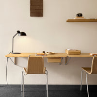 Natural wood desk and light-colored wall with minimalist black and metallic accents, featuring neutral-toned chairs.