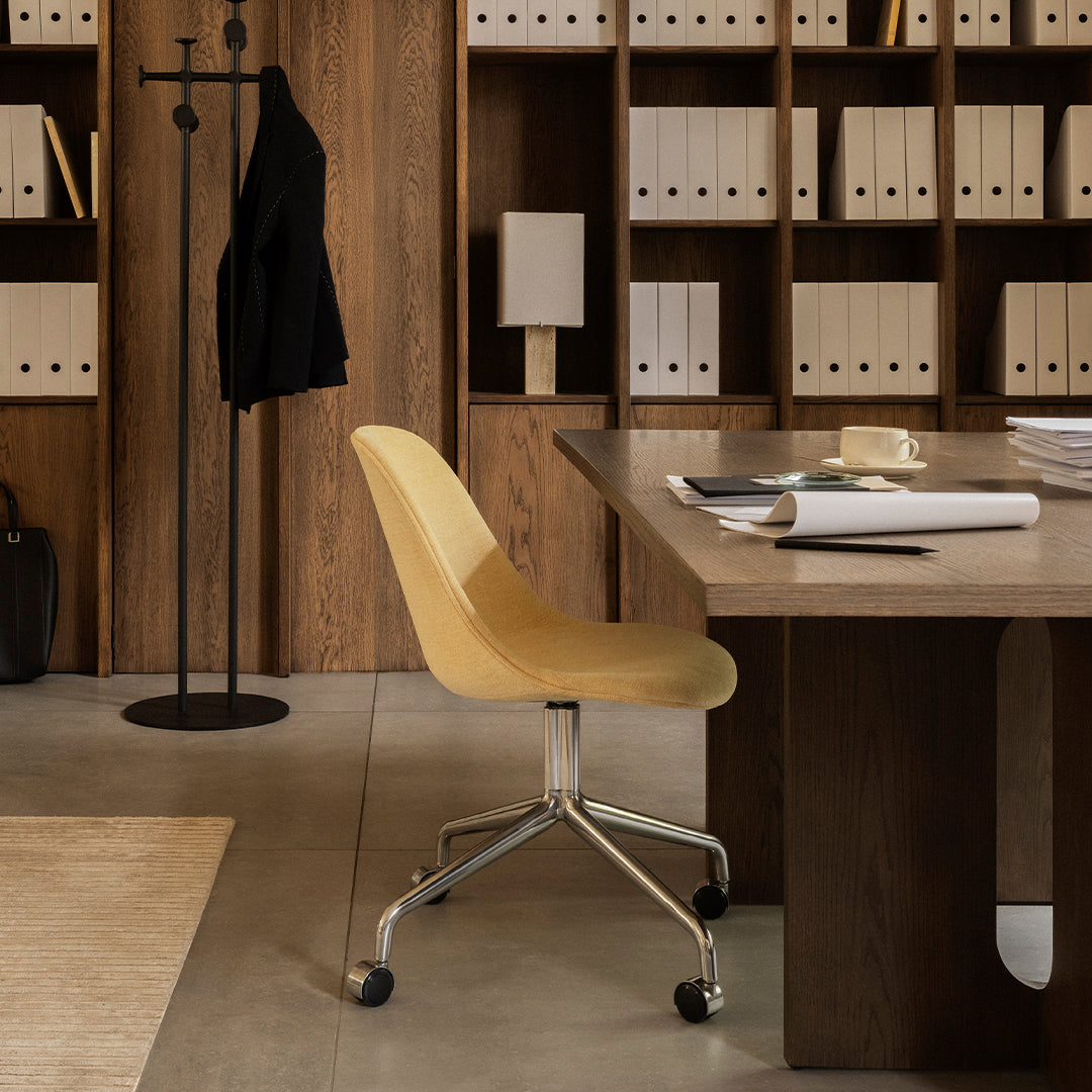 Yellow ergonomic chair on a sleek silver base, set against a warm wooden backdrop with neutral tones and soft textures.
