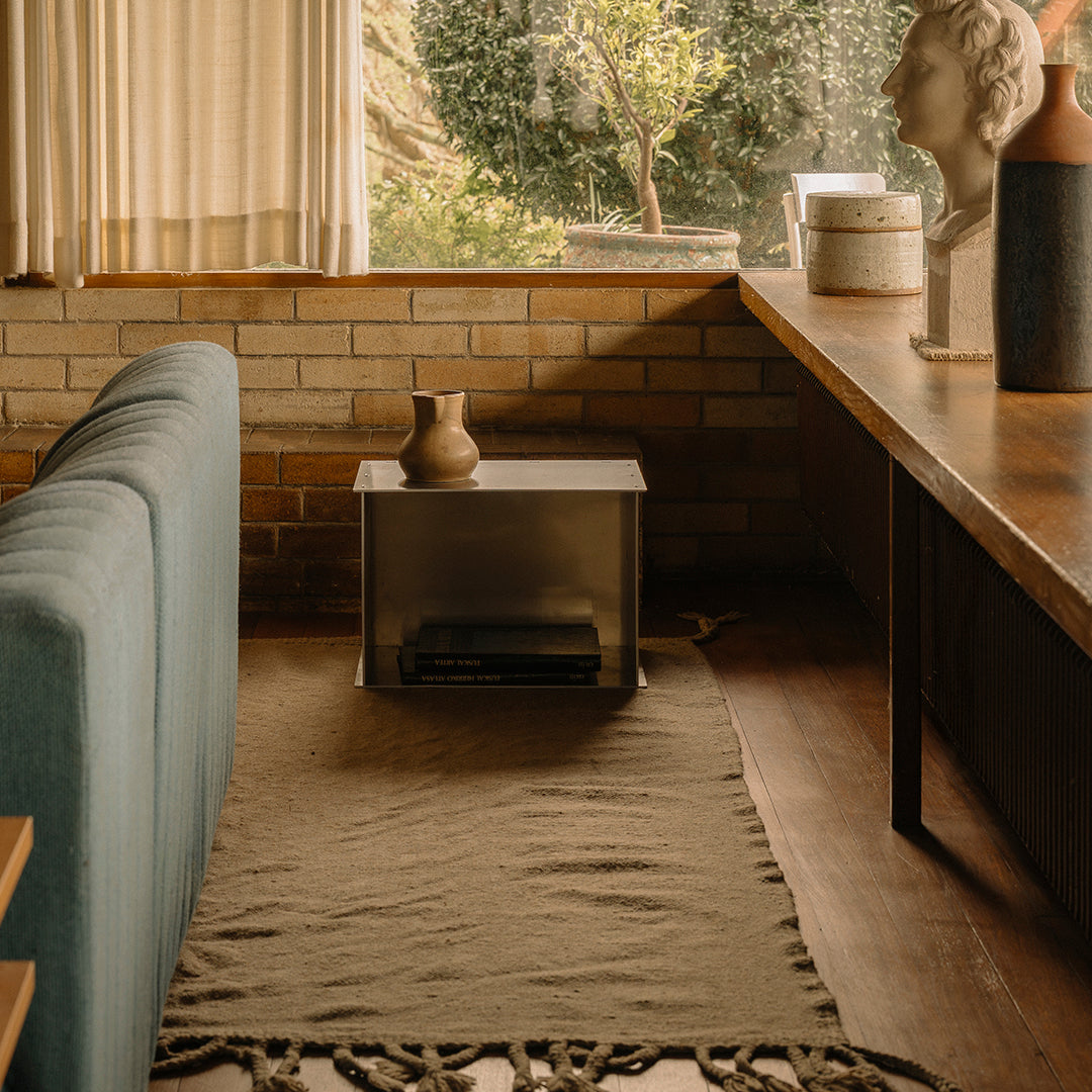 Cozy living space featuring a soft beige rug with fringe, teal couch, and warm earth-toned decor elements.