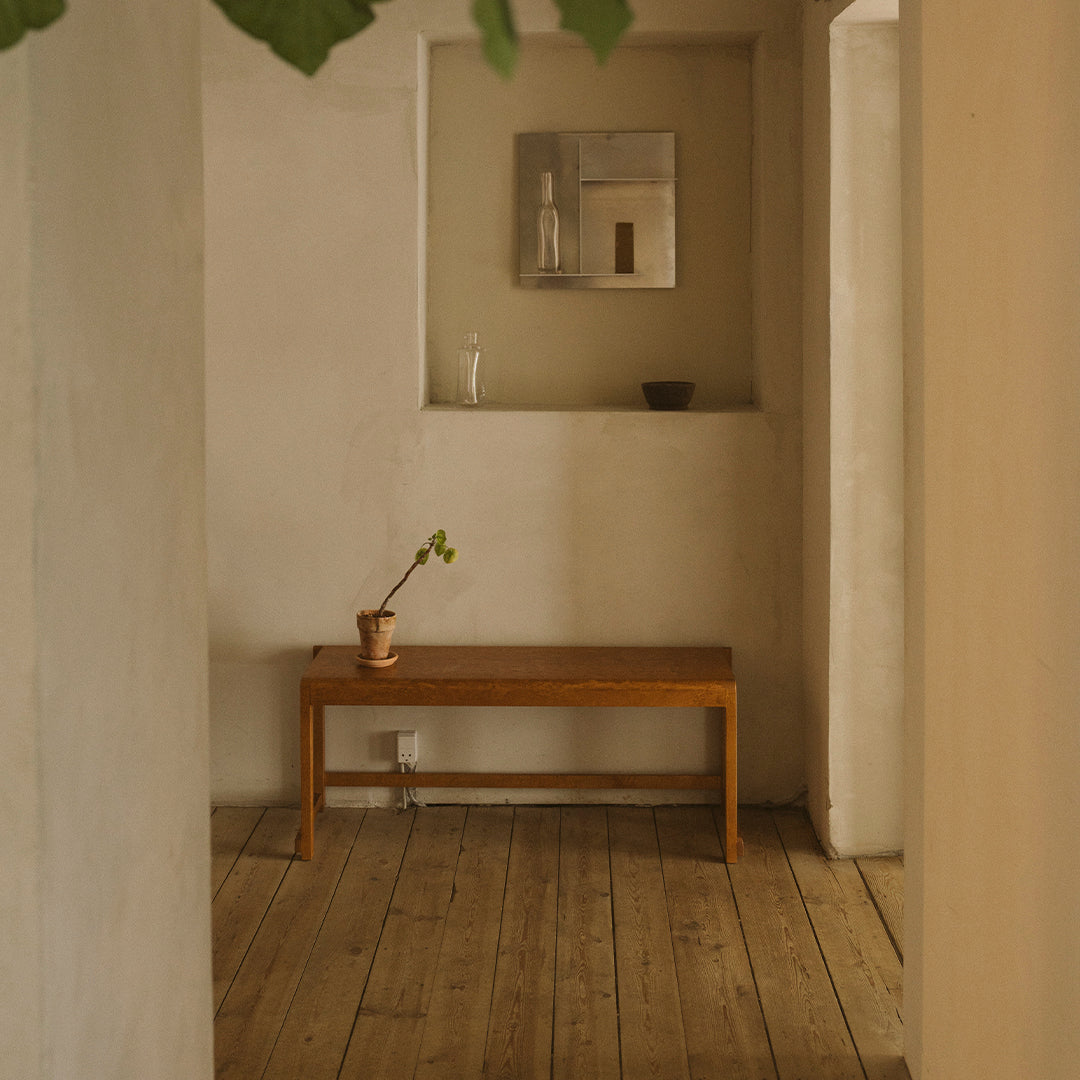 Wooden bench with warm tones, set against neutral-colored walls and a light wood floor, creating a serene, minimal aesthetic.