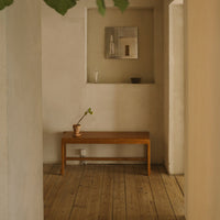 Wooden bench with warm tones, set against neutral-colored walls and a light wood floor, creating a serene, minimal aesthetic.