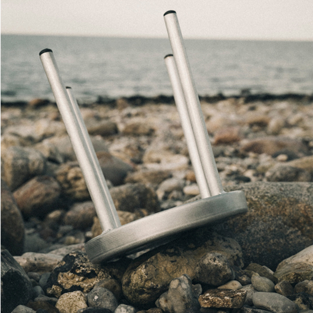 Silver metal stool legs on a rocky beach, showcasing a sleek, modern design against natural earthy tones.