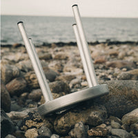 Silver metal stool legs on a rocky beach, showcasing a sleek, modern design against natural earthy tones.
