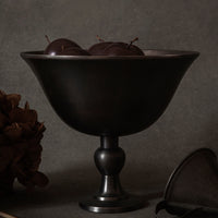 Black decorative bowl with polished finish, featuring dark brown accents and glossy chocolate-colored fruit inside.
