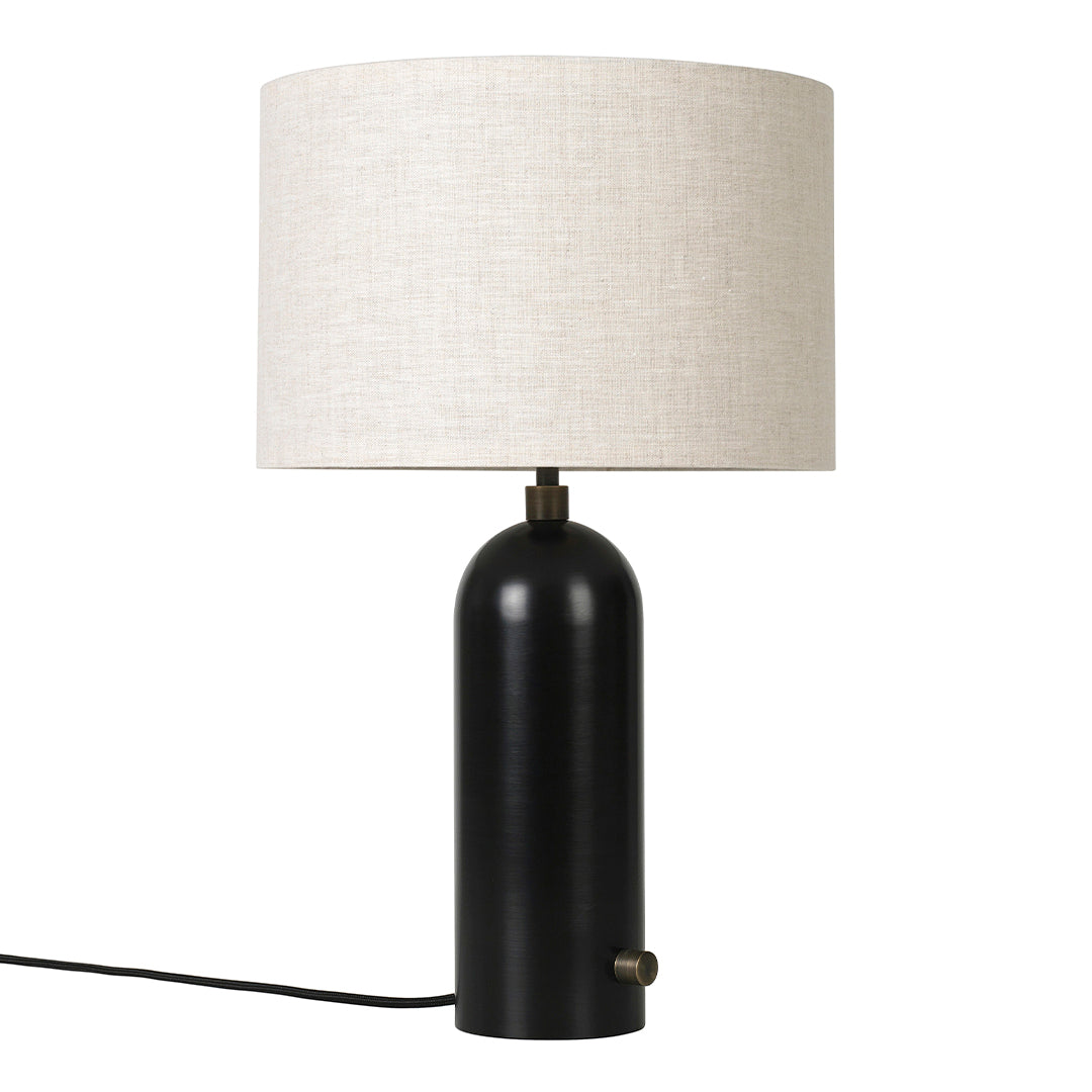 Black cylindrical lamp base with a cream linen shade, featuring a sleek, minimalist design and brass accents.