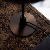 Bronze lamp base on a textured dark granite surface with natural earthy tones and subtle veining patterns.
