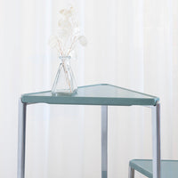 Triangular table with a soft green surface and chrome legs, showcasing a modern minimalist design.