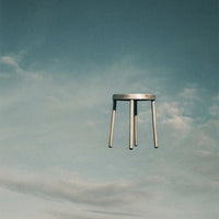 Minimalist metal stool against a soft blue sky with wispy white clouds, showcasing a sleek, modern design.
