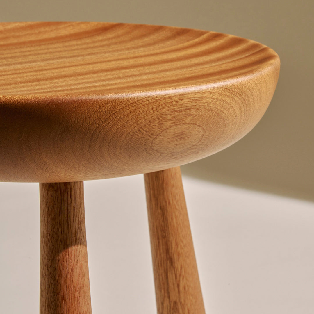 Natural wood stool with light brown tones and a smooth, rounded top featuring subtle, wavy grain patterns.