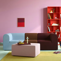 Multi-colored sofa in blue, brown, and burgundy, with a pink coffee table against a soft pink wall. Bright red shelf accents.