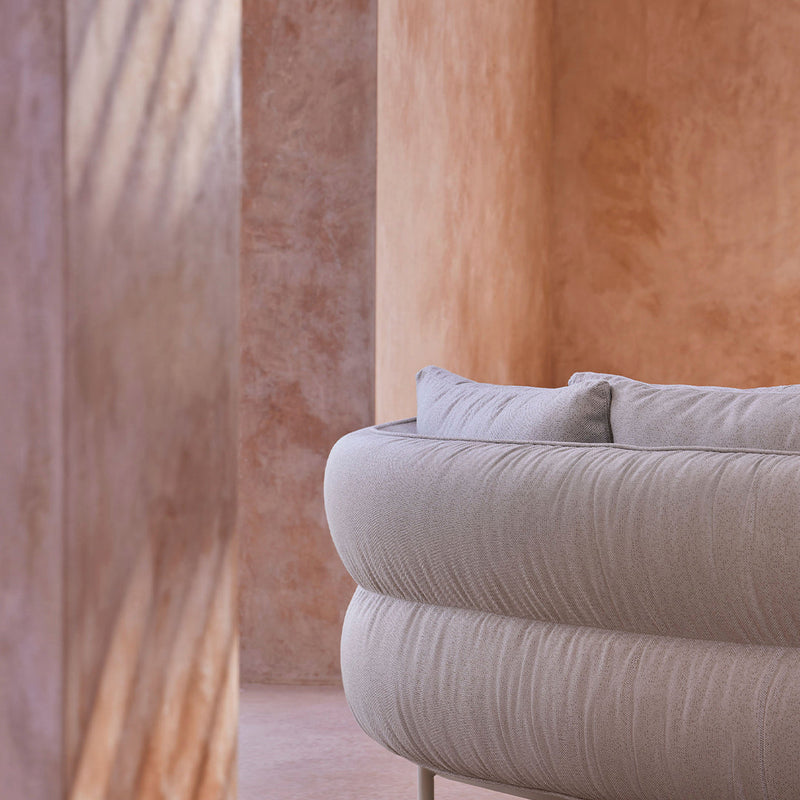 Soft gray circular sofa against warm, textured peach walls, creating a cozy modern aesthetic.