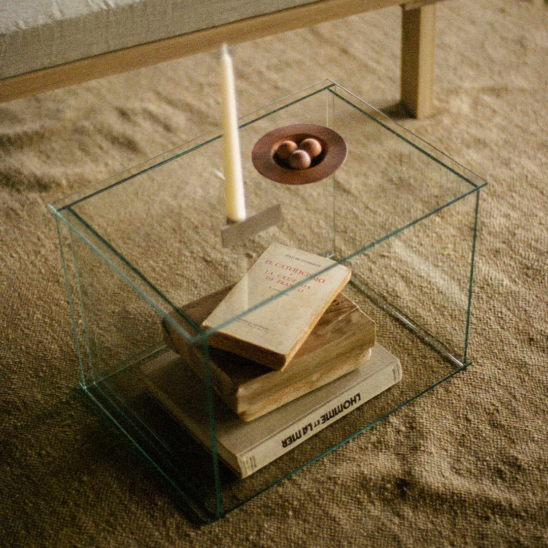 Clear glass display table with minimalist design, featuring natural wood tones and soft beige textures.