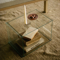 Clear glass display table with minimalist design, featuring natural wood tones and soft beige textures.