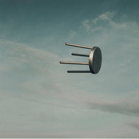 Floating gray stool with a smooth, circular top and three metallic legs against a soft blue sky.