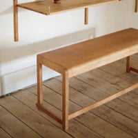 Natural wood bench with a smooth, light oak finish, featuring minimalist design and clean lines on a rustic wooden floor.