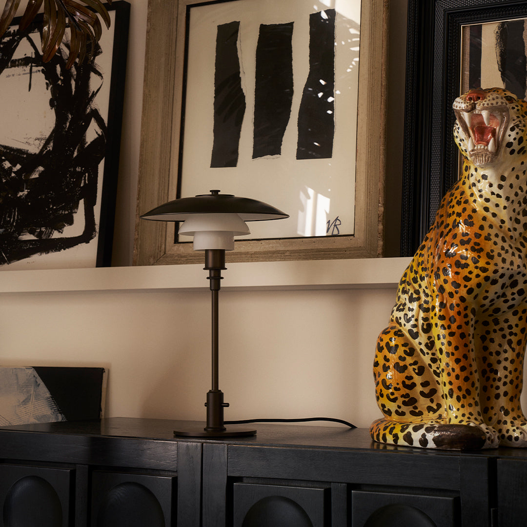 "Black and white abstract art, golden leopard statue, and sleek black lamp on a dark wooden console table."