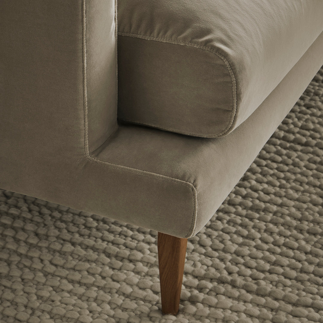 Light taupe velvet sofa with clean lines and wooden legs, paired with a textured gray woven rug.
