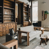 Modern beige sofa with wooden accents, surrounded by dark wood shelves and light-colored floors, creating a warm ambiance.