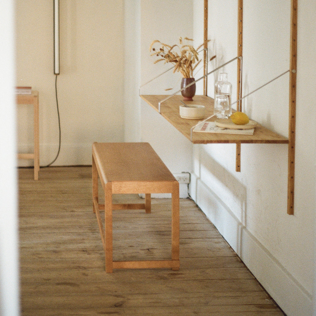 Light wood bench with a minimalist design, set against a neutral backdrop, complemented by a warm wooden floor.