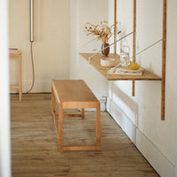 Light wood bench with a minimalist design, set against a neutral backdrop, complemented by a warm wooden floor.