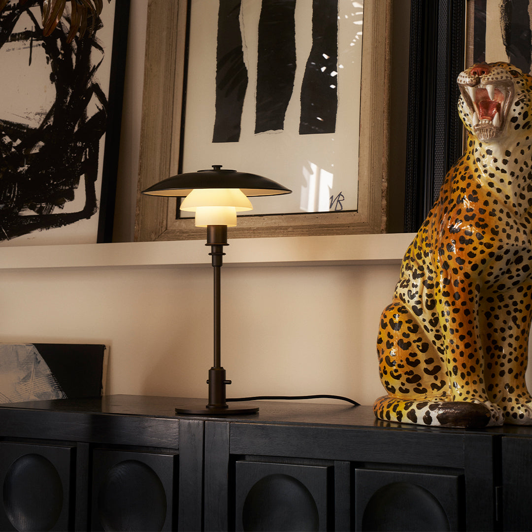 "Black and gold table lamp with a white glass shade, accompanied by a vibrant, spotted leopard statue."