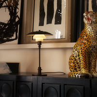 "Black and gold table lamp with a white glass shade, accompanied by a vibrant, spotted leopard statue."