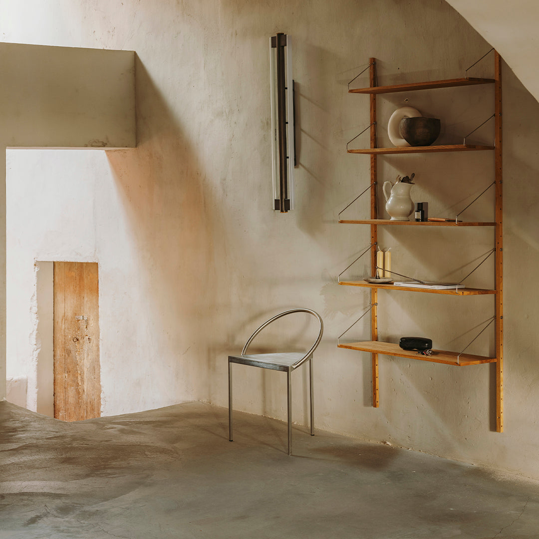 Modern minimalist room with warm beige walls, wooden shelving, and a clear acrylic chair. Soft, neutral tones throughout.