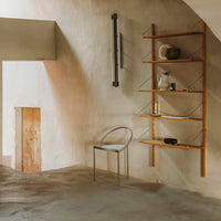 Modern minimalist room with warm beige walls, wooden shelving, and a clear acrylic chair. Soft, neutral tones throughout.