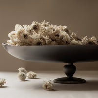 Black bowl filled with cream-colored flowers against a neutral background, with scattered floral accents.
