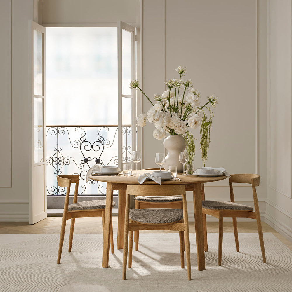 Light beige walls, natural wood table and chairs, soft gray upholstery, white floral arrangements, and a neutral rug.