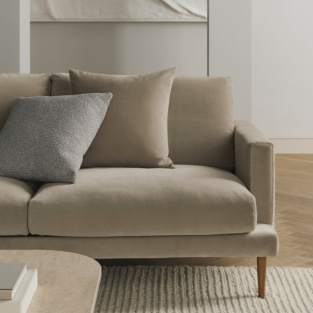 Light beige sofa with a textured gray pillow, featuring clean lines and a minimalist style on a light wood floor.