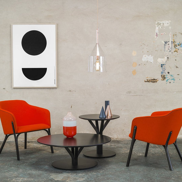 Modern living room with bold orange chairs, black circular tables, and minimalist black and white wall art.