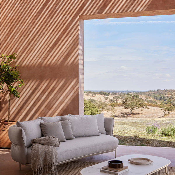 Light gray couch with textured cushions against a warm, earthy-toned backdrop and natural landscape view.