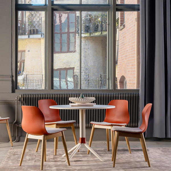 Modern dining set featuring warm orange chairs, light wood accents, and a sleek white table against a neutral backdrop.