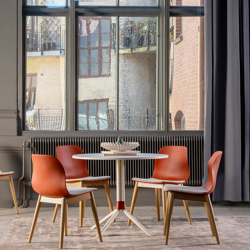 Modern dining set featuring warm orange chairs, light wood accents, and a sleek white table against a neutral backdrop.