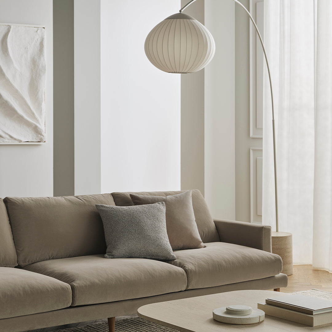 Neutral beige sofa with a grey accent pillow, paired with soft white decor and light, airy curtains.