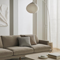 Neutral beige sofa with a grey accent pillow, paired with soft white decor and light, airy curtains.