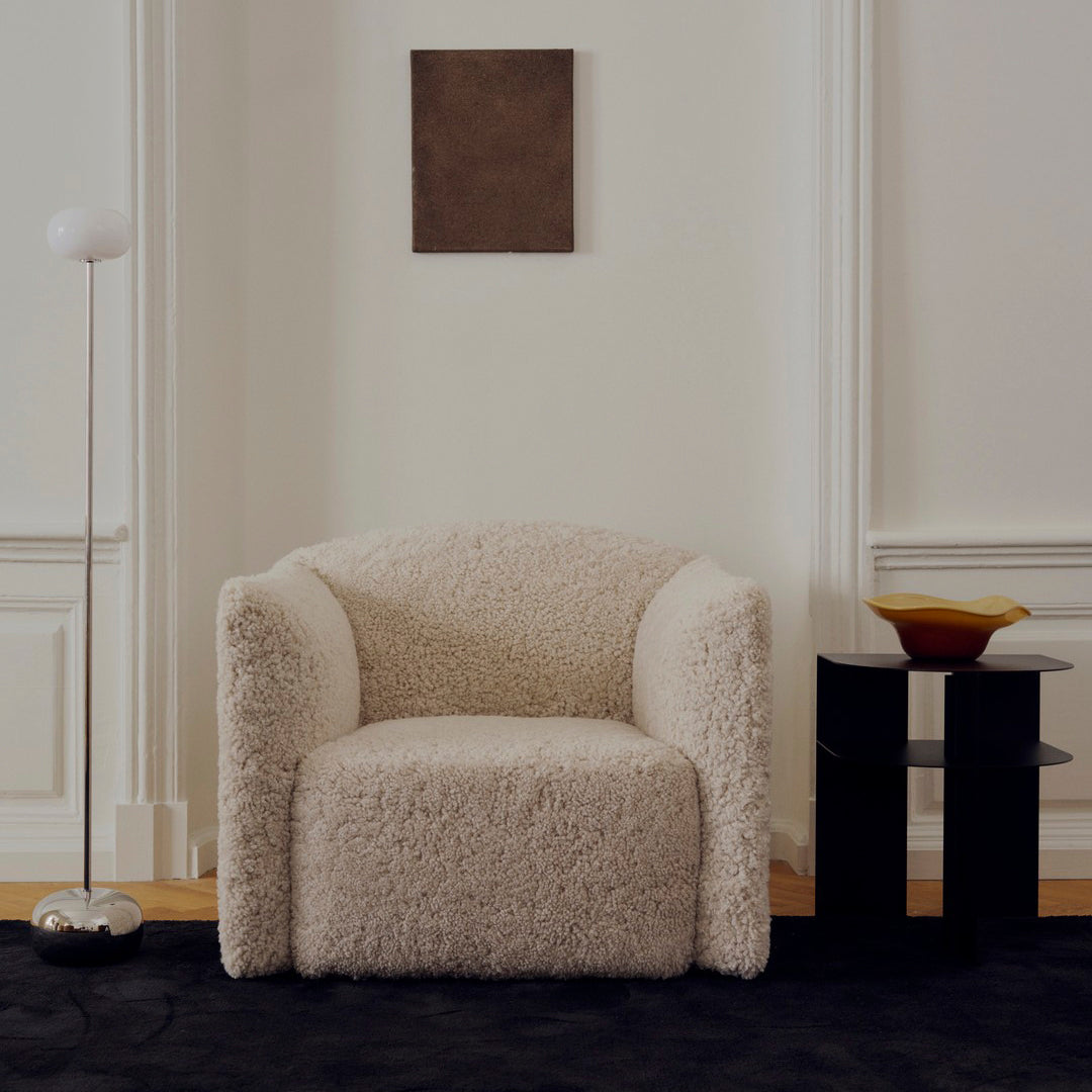 Cozy cream-colored armchair with a soft, textured finish, set against a sleek black rug and minimalist decor.
