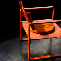 Vibrant orange armchair with sleek lines and round cushion, set against a dark background, highlighting its modern design.