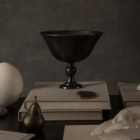 Dark bronze bowl atop stacked gray books, featuring a sleek, modern design with a smooth finish. Elegant home decor.