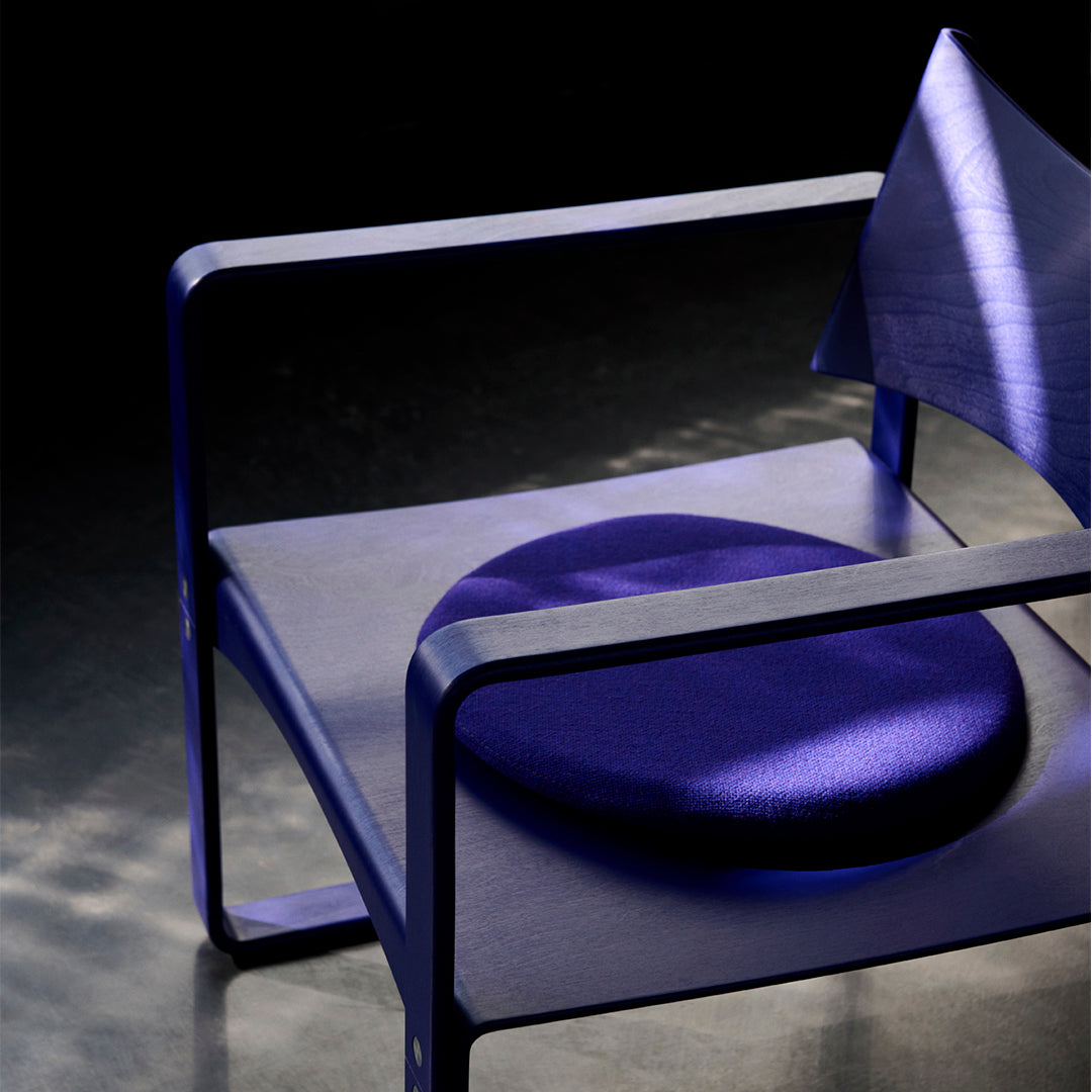 Vibrant purple chair with a round, plush cushion and sleek geometric design against a dark backdrop.