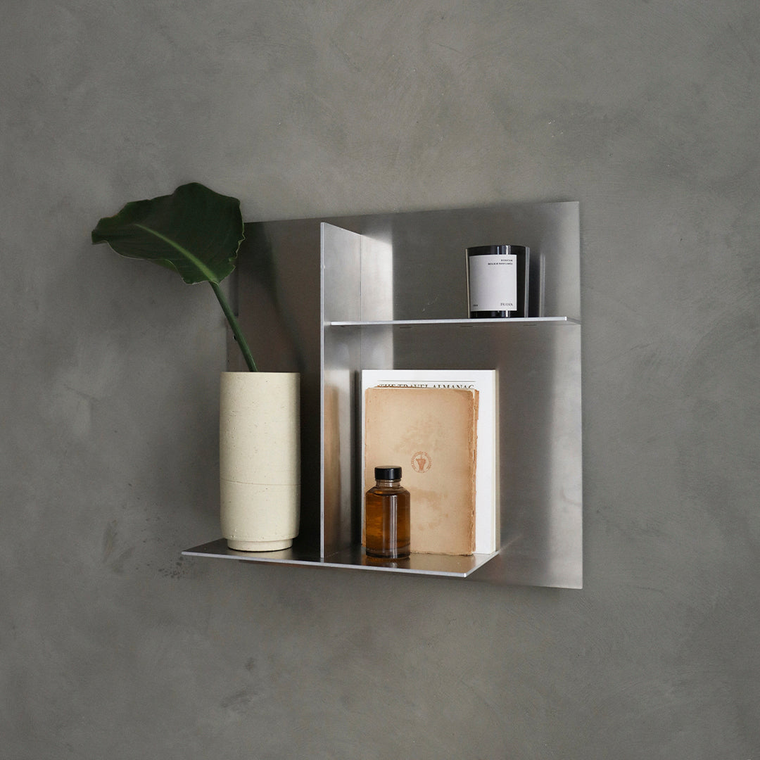 Modern silver shelf with sleek lines, featuring a neutral beige vase, black and white decor items, against a gray background.