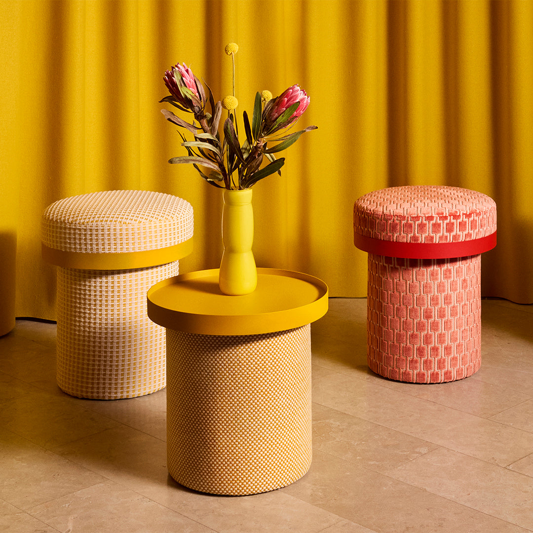 Colorful dining stools in yellow, pink, and cream patterns against a vibrant yellow backdrop.