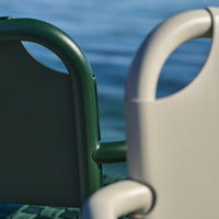 Green and gray outdoor chairs with smooth, rounded armrests against a water backdrop.