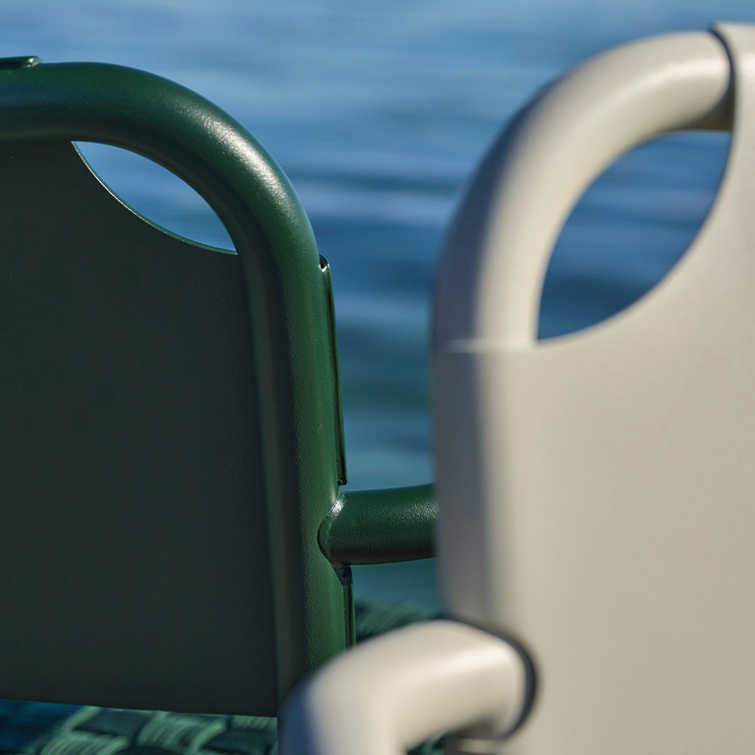 Green and gray outdoor chairs with sleek, minimalist design against a tranquil water background.