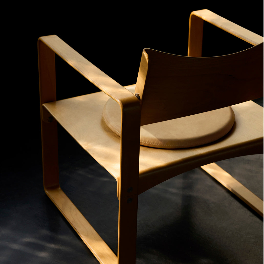 Light wood armchair featuring smooth curves and a natural finish against a dark background.