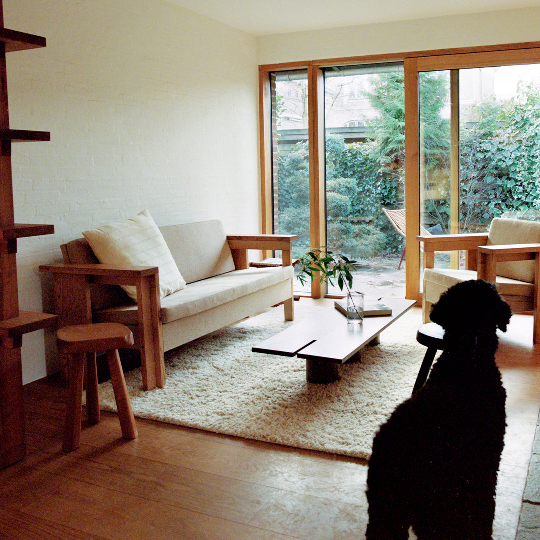 Cozy living room with natural wood tones, soft beige upholstery, and a light-colored rug against a green garden backdrop.